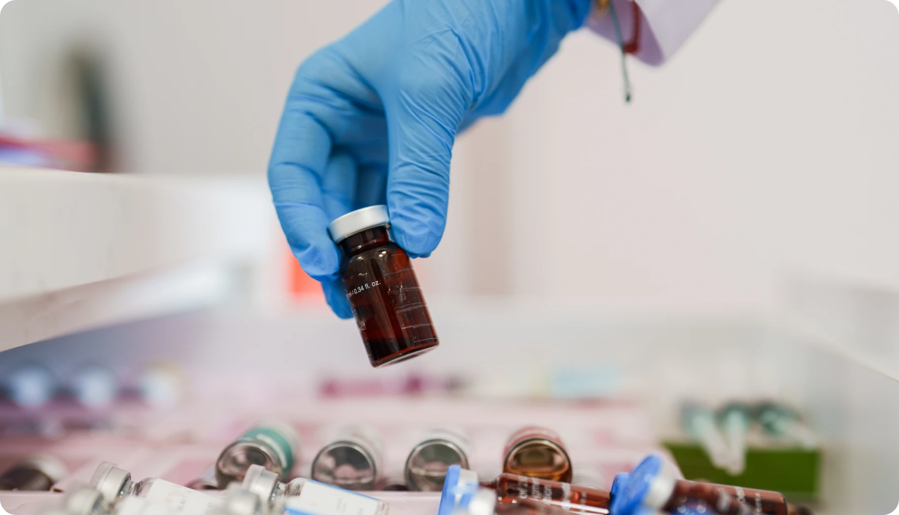 Gloved hand holding a small medical vial.